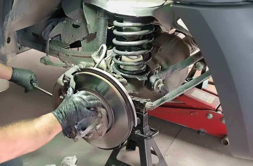 Reemplazo de frenos de disco y pastillas por un mecánico, con el coche asegurado con una borriqueta, mostrando el muelle de la suspensión