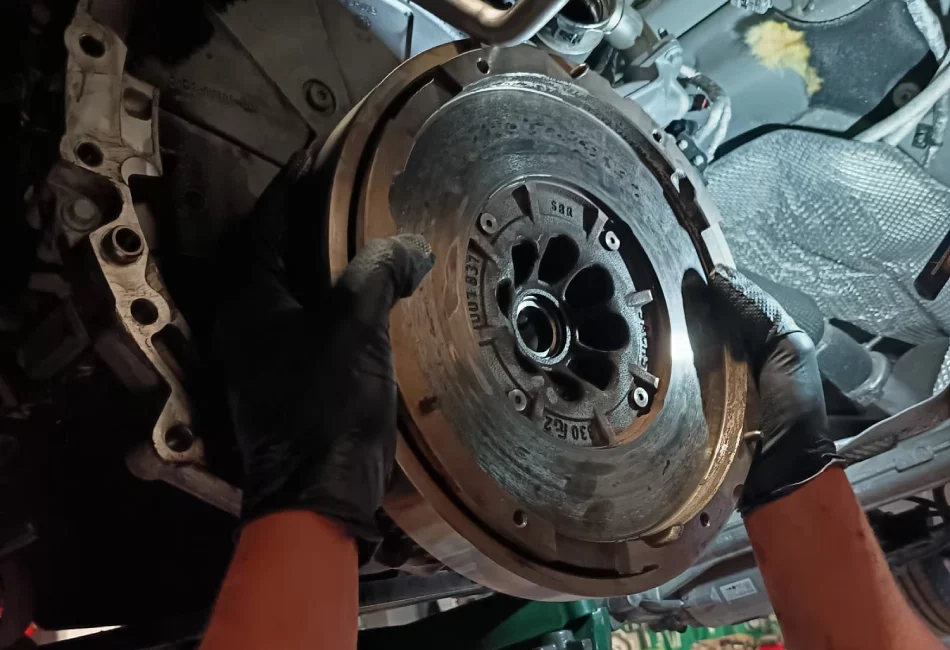 Mecánico reemplazando un volante de motor en un coche, con guantes negros y herramientas visibles en un taller mecánico profesional