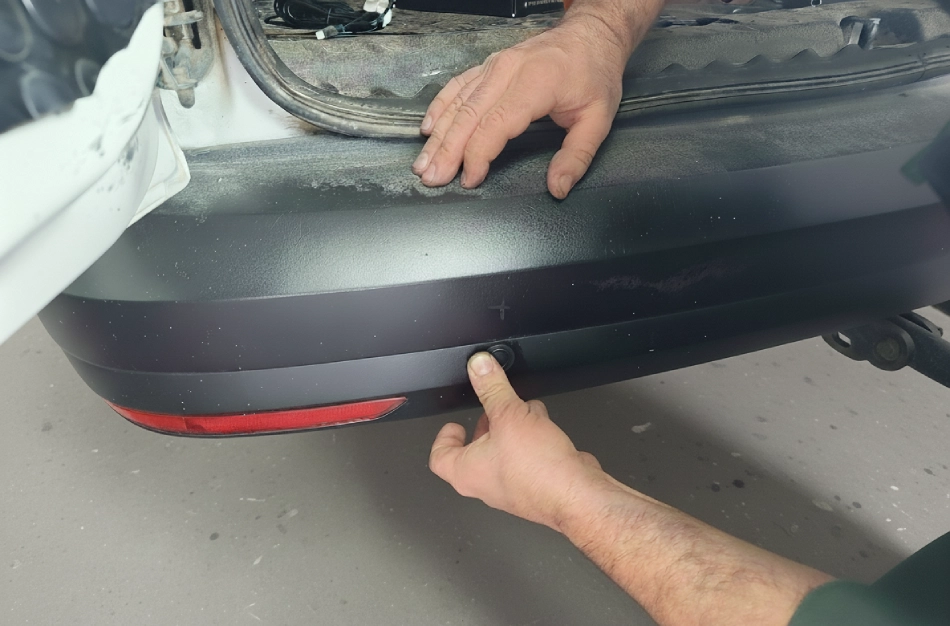 Técnico instalando un sensor de aparcamiento trasero en el parachoques de un vehículo